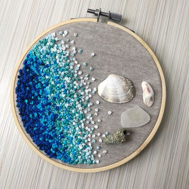 a close up of a embroidery on a table with shells and sea glass in it