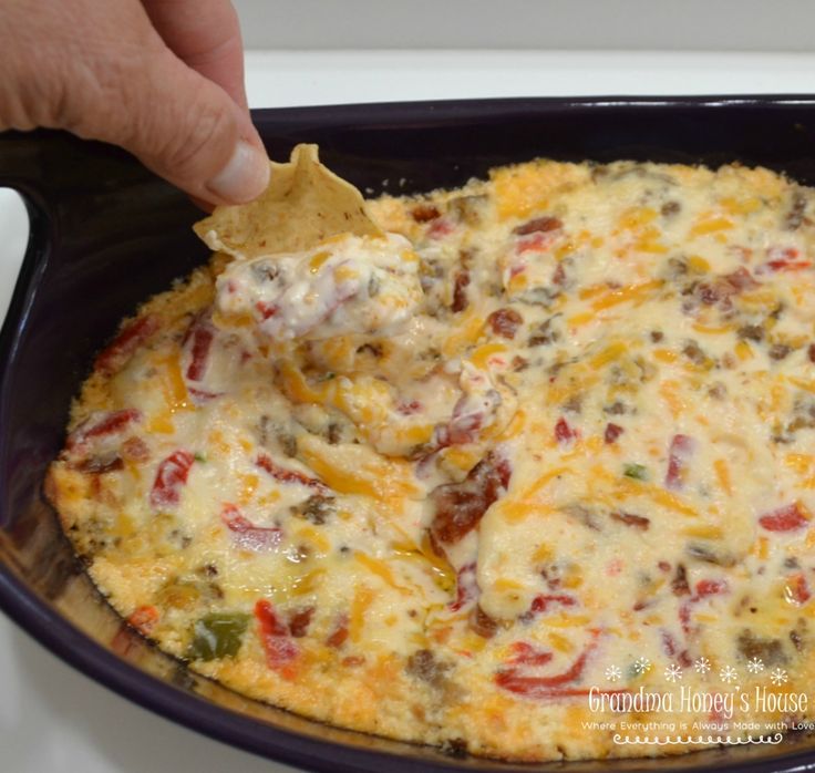 a hand dipping a tortilla chip into a casserole dish with cheese and vegetables