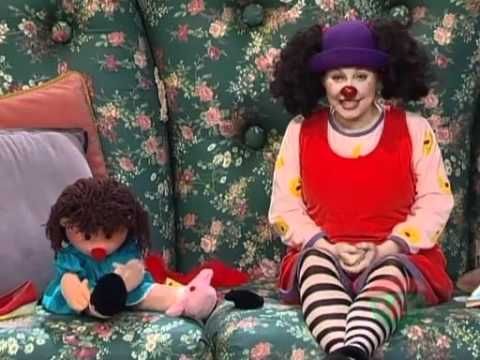 a clown sitting on top of a couch next to two stuffed animals