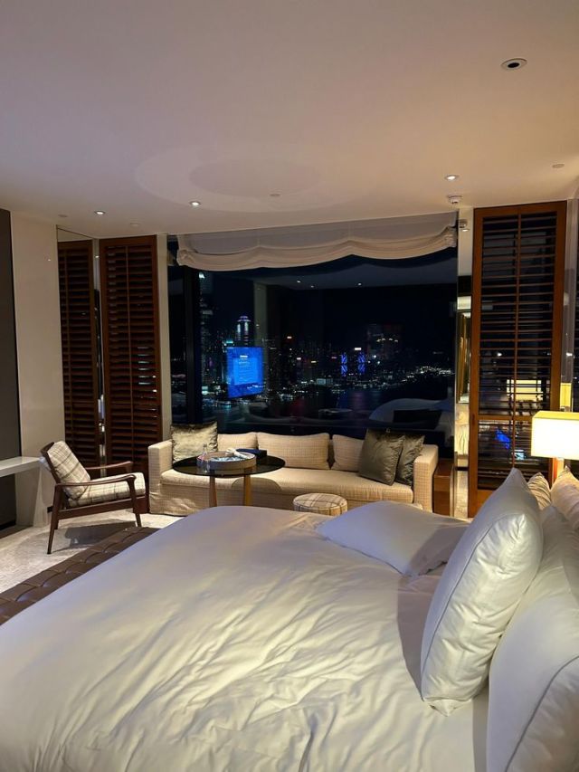 a large white bed sitting in a bedroom next to a window with city lights on it