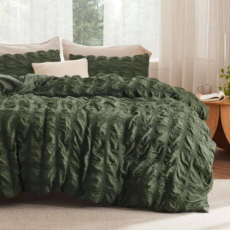 a bed with green comforter and pillows in a room next to a window,