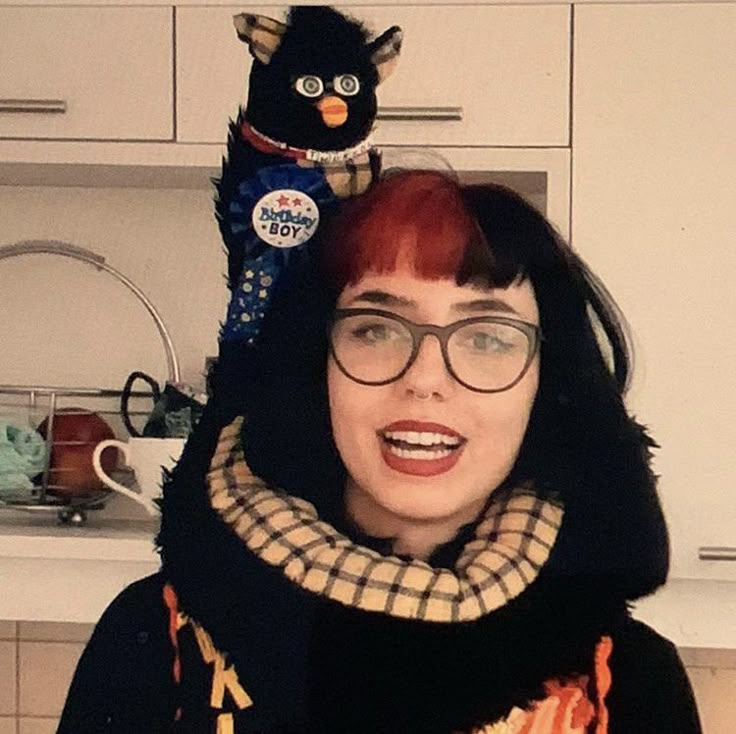 a woman with red hair wearing glasses and a scarf around her neck standing in front of a kitchen counter