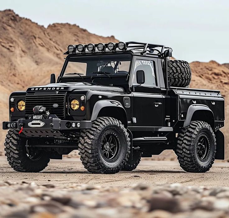 a large black truck parked on top of a dirt field next to rocks and mountains