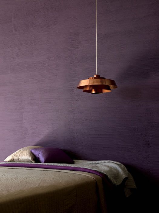 a bedroom with purple walls and a bed in the foreground is a lamp hanging from the ceiling