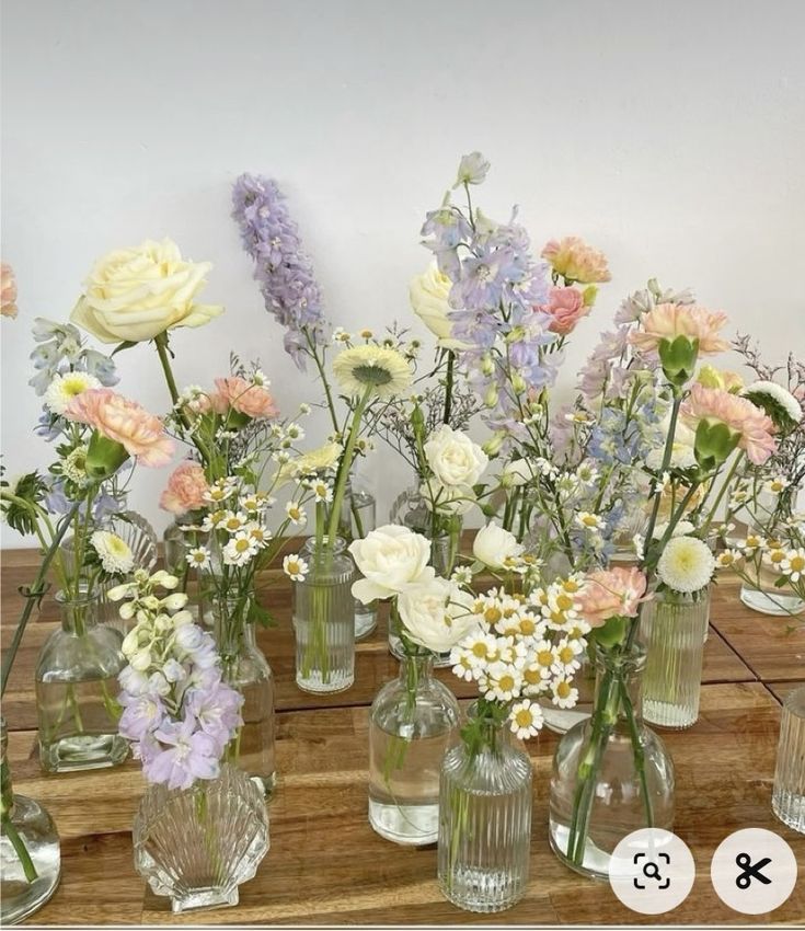 there are many different vases with flowers in them on the wooden table next to each other