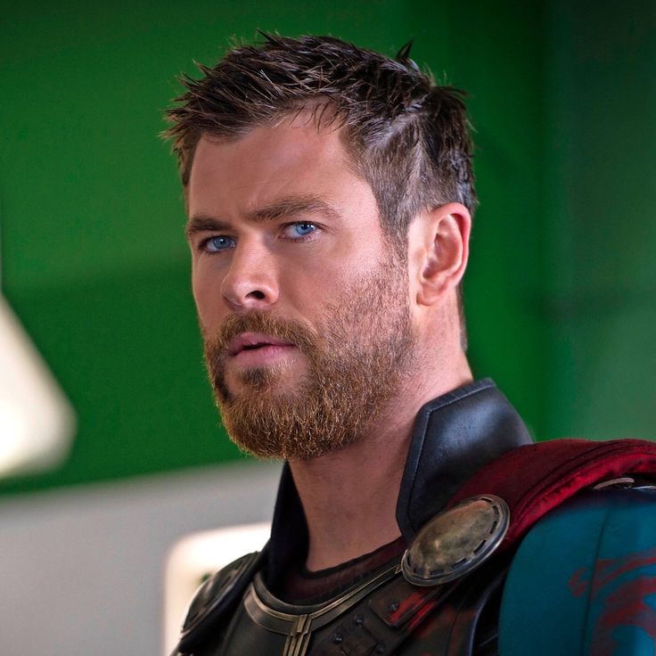 a close up of a person with a beard and wearing a costume in front of a green wall