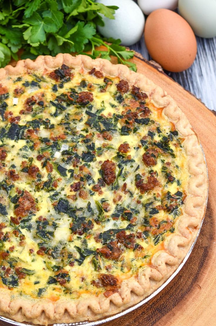 a quiche with spinach, cheese and other ingredients on a wooden board next to eggs