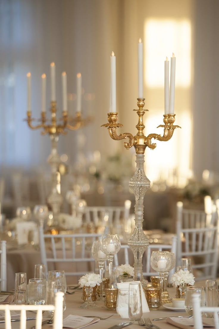 the centerpieces on this table are all gold and white, with candles in them