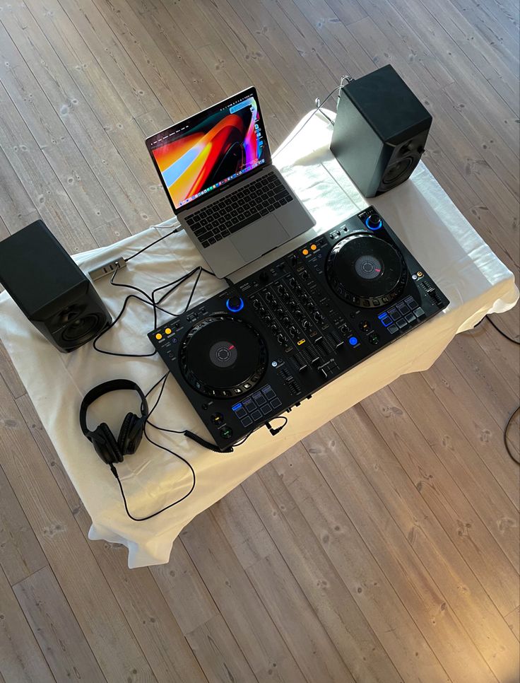 a laptop computer sitting on top of a table next to dj's controllers and headphones