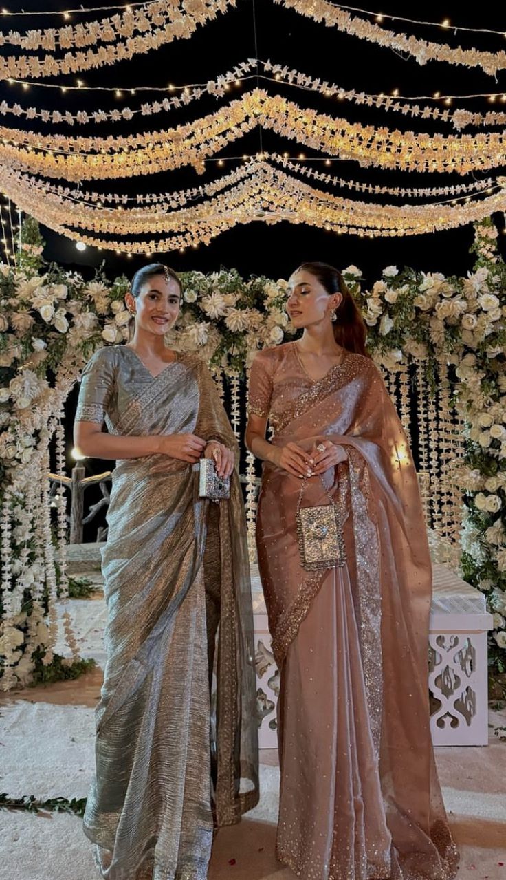 two women standing next to each other in front of a flower covered stage with lights