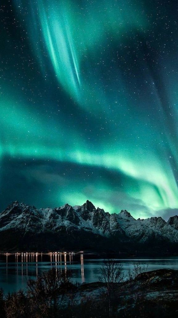 the northern lights shine brightly in the night sky over water and mountains with snow on them