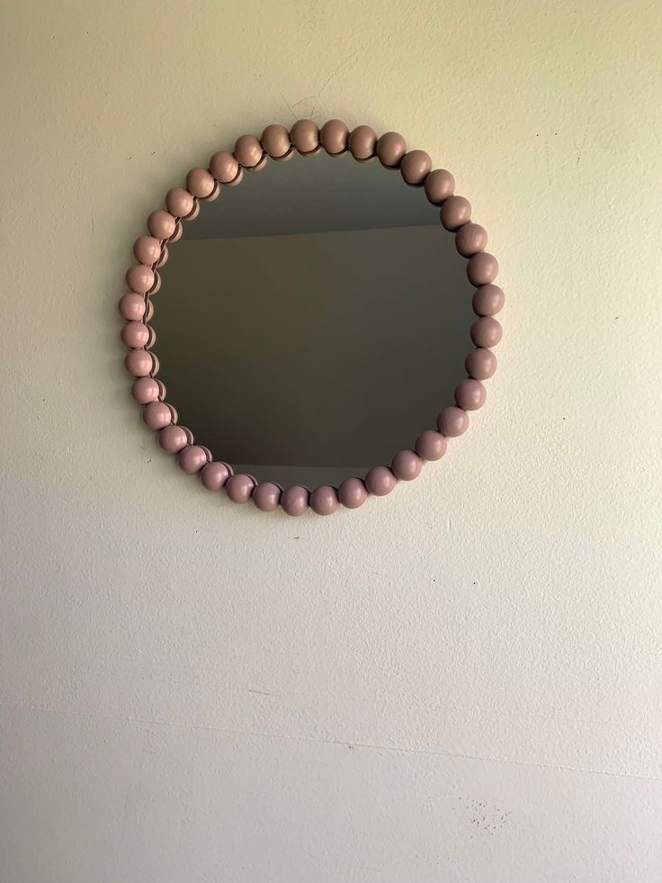 a round mirror mounted on the wall above a wooden bead necklace hanging from a hook