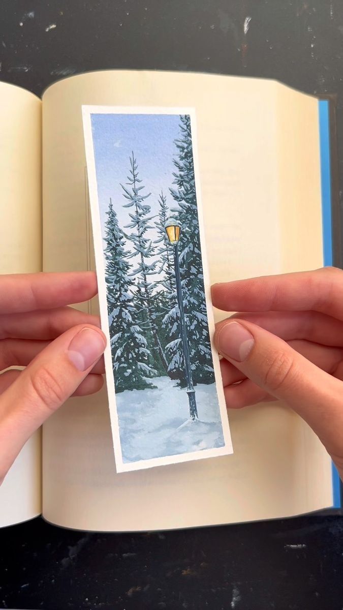 a person holding up an open book with a picture of a street light in the snow