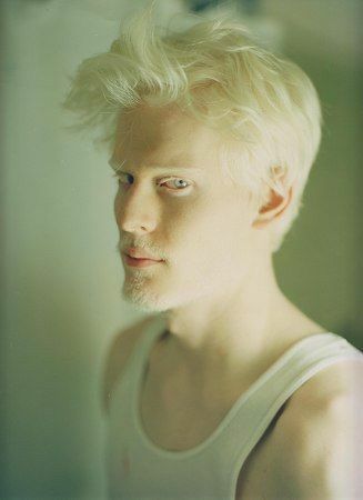 a man with blonde hair is looking at the camera while wearing a white tank top