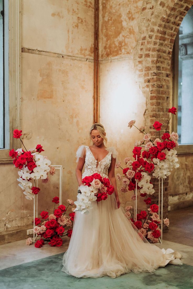 a woman in a wedding dress standing next to red and white flowers