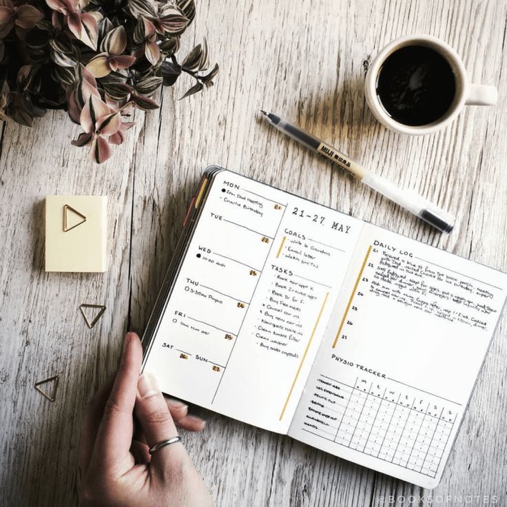 a person's hand is holding an open planner next to a cup of coffee