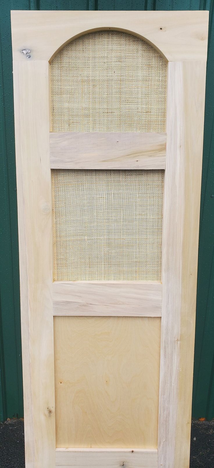 an unfinished wooden door with mesh screen on the front and side panels, sitting against a green wall