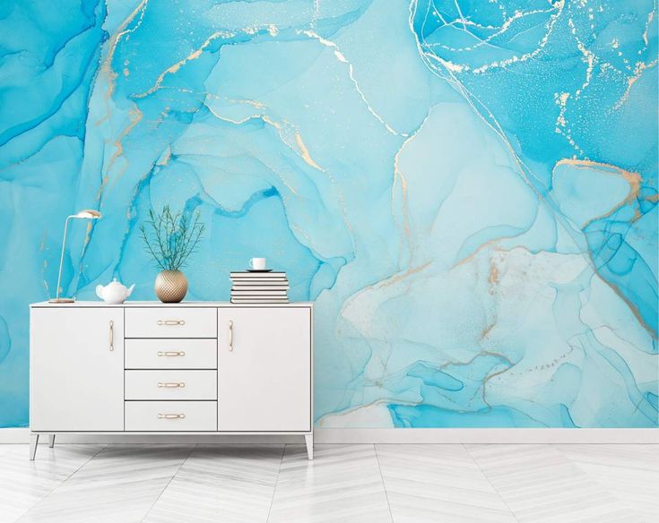 a white cabinet sitting in front of a blue and gold wallpapered room with an abstract painting on the wall