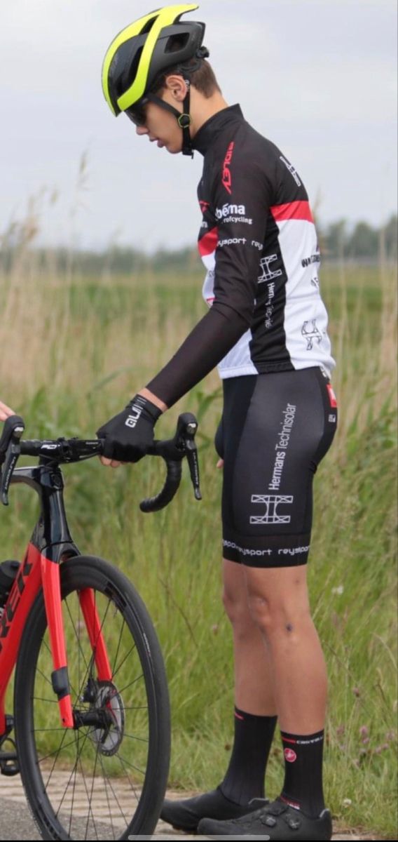 a man standing next to his bike on the side of a road in front of tall grass