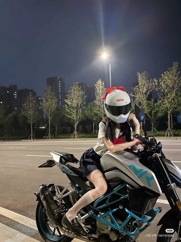 a woman riding on the back of a silver motorcycle at night with city lights in the background