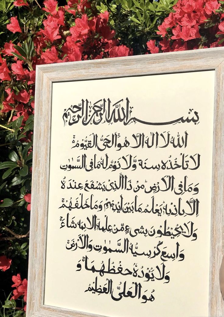 an arabic calligraphy displayed in front of red flowers