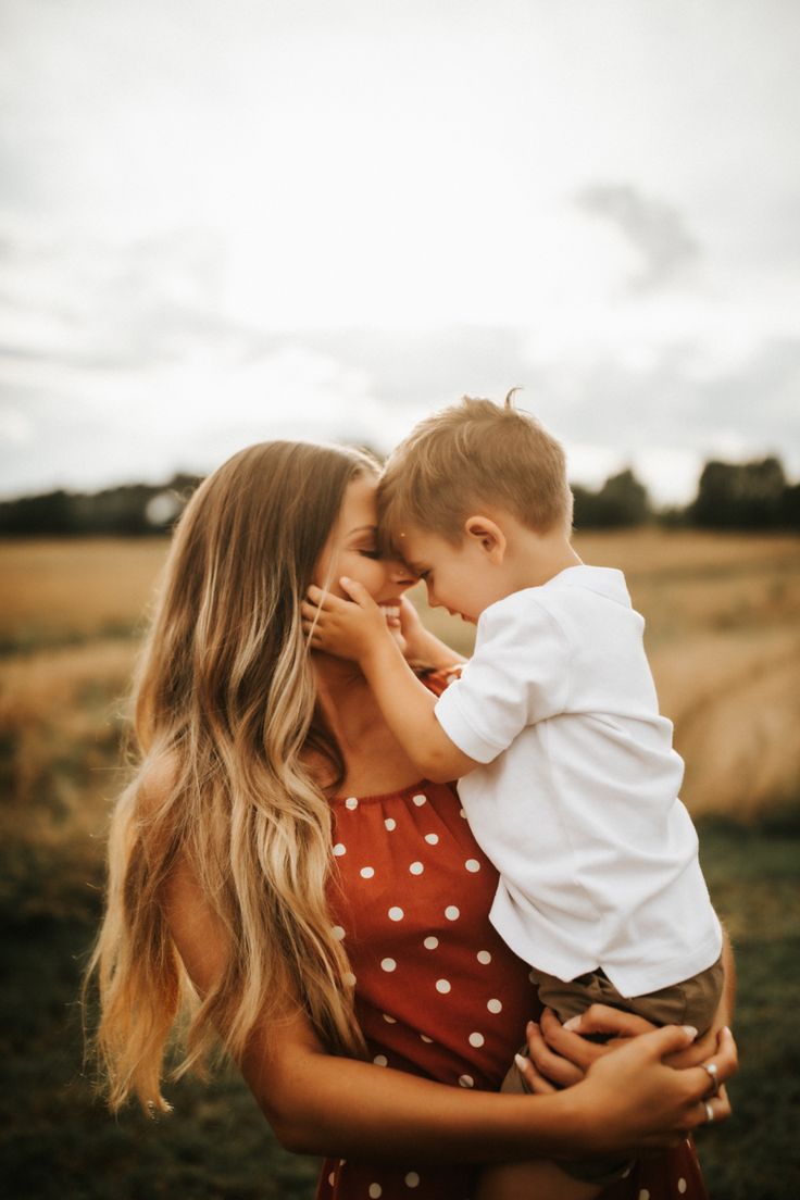 a woman holding a young boy in her arms while he is kissing him on the cheek