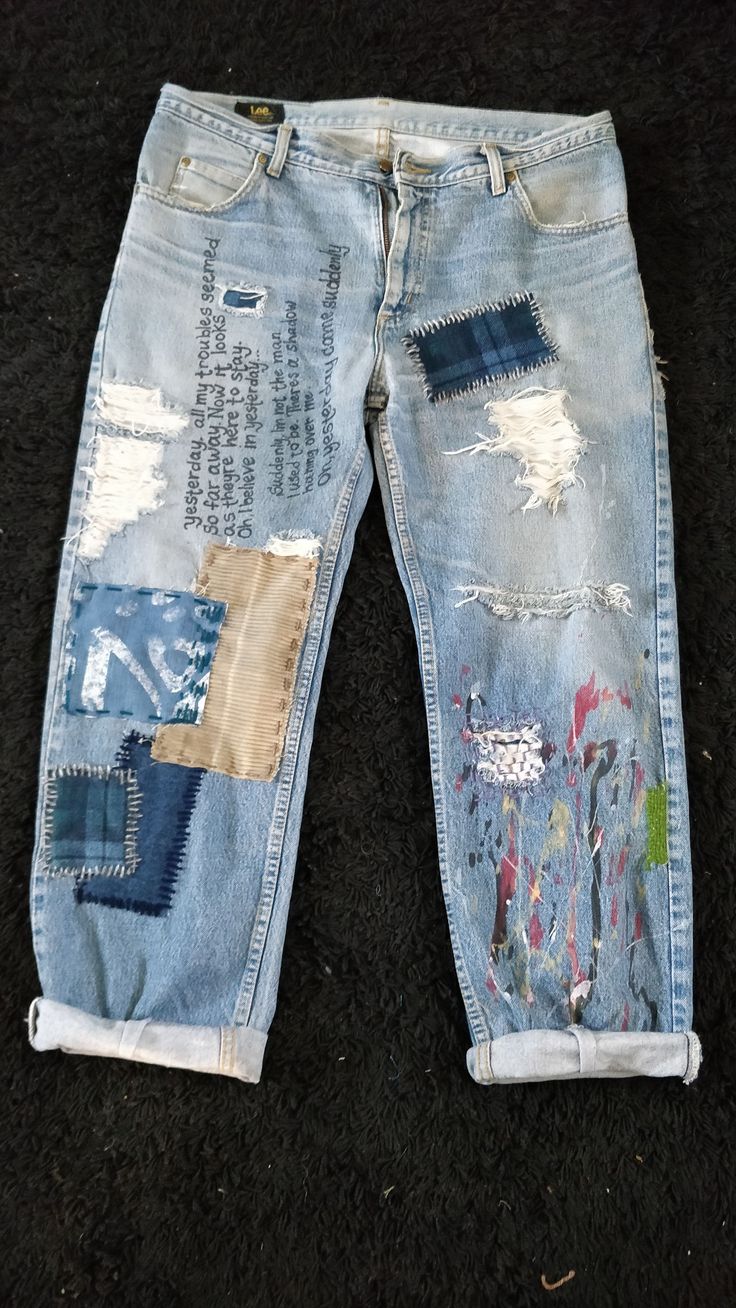 an old pair of jeans with patches and paint on them sitting on the ground in front of a black carpet