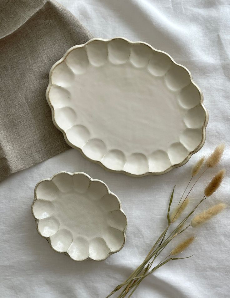 two white plates sitting on top of a bed next to each other and some dried grass