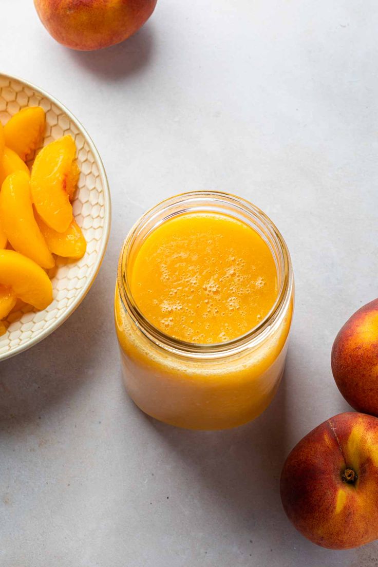 a bowl of peaches next to a jar of orange juice on a white table