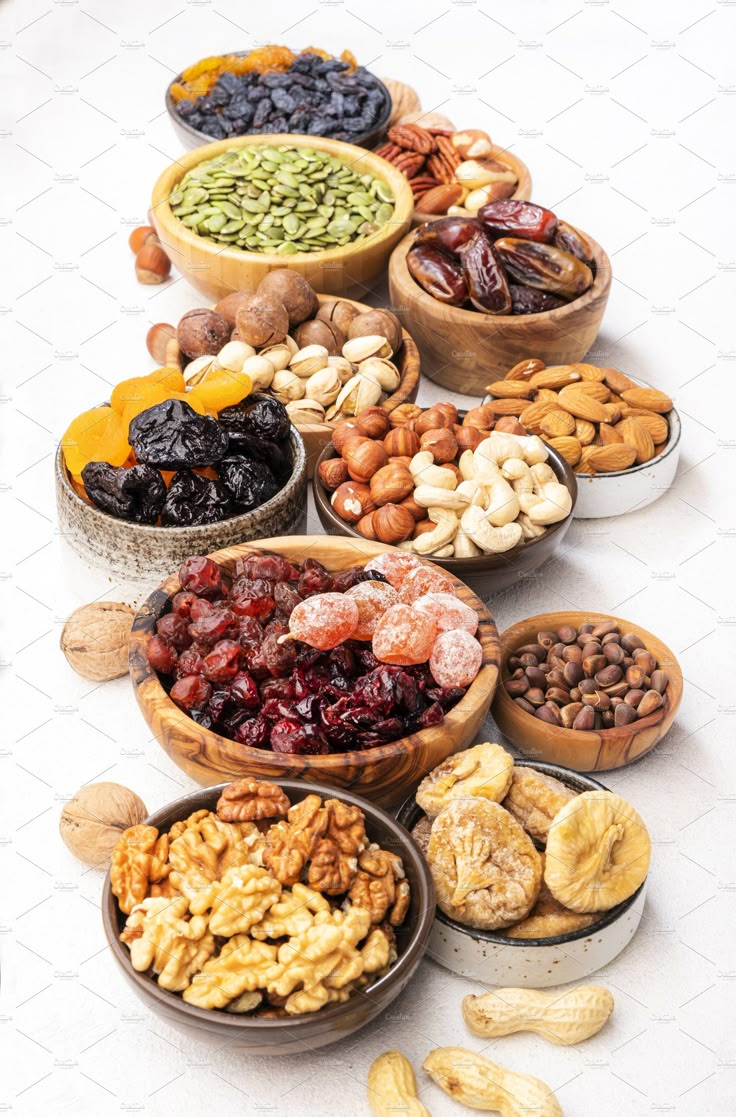 a number of bowls filled with different types of nuts and dried fruits on a white surface