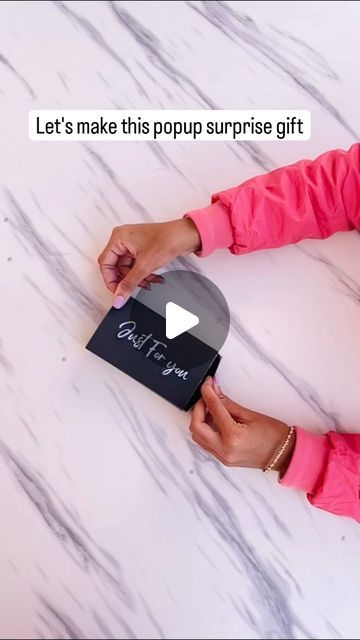 a woman holding a black box on top of a white table with text that reads let's make this popup surprise gift