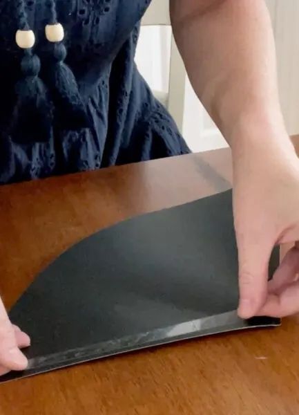 a person with their hand on top of a piece of black paper that is sitting on a table