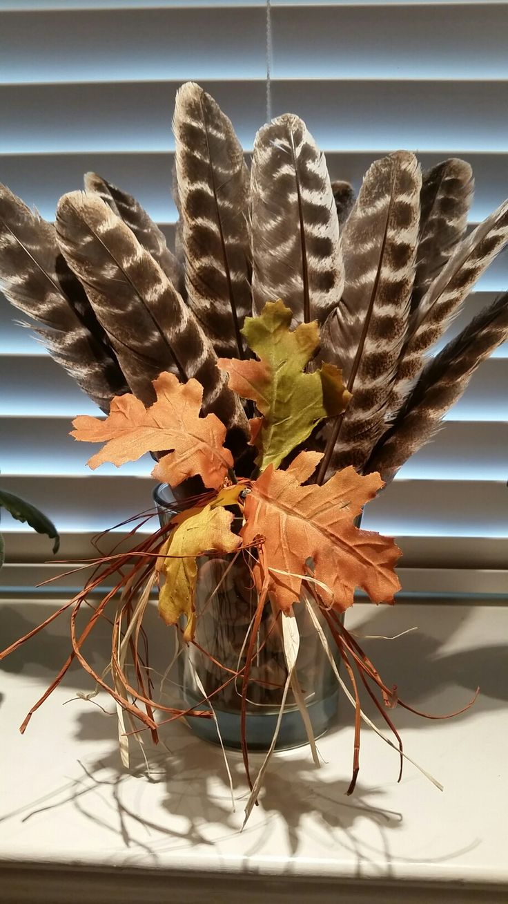 a vase filled with feathers and leaves on top of a window sill