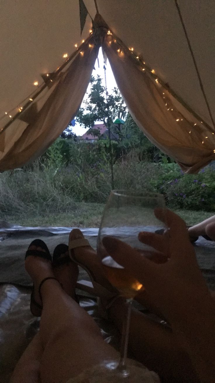 someone holding a wine glass in their hand while sitting under a tent with lights on it