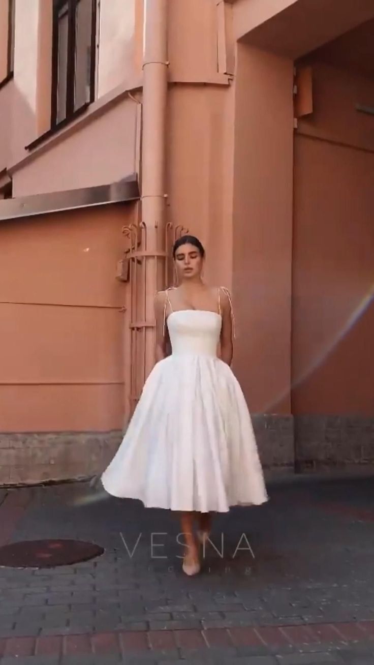 a woman standing in front of a building wearing a white dress