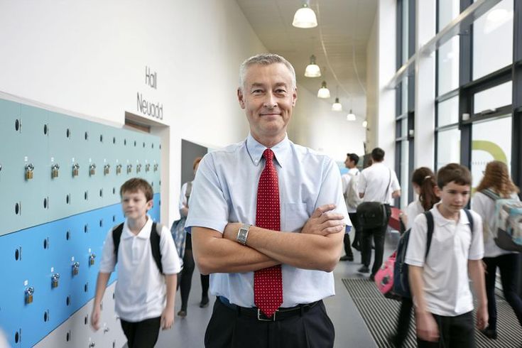 a man with his arms crossed standing in front of schoolchilds wearing white shirts and red ties