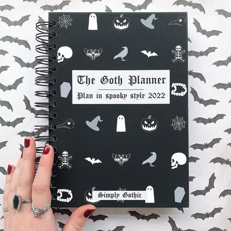 a woman's hand holding up a black and white halloween planner