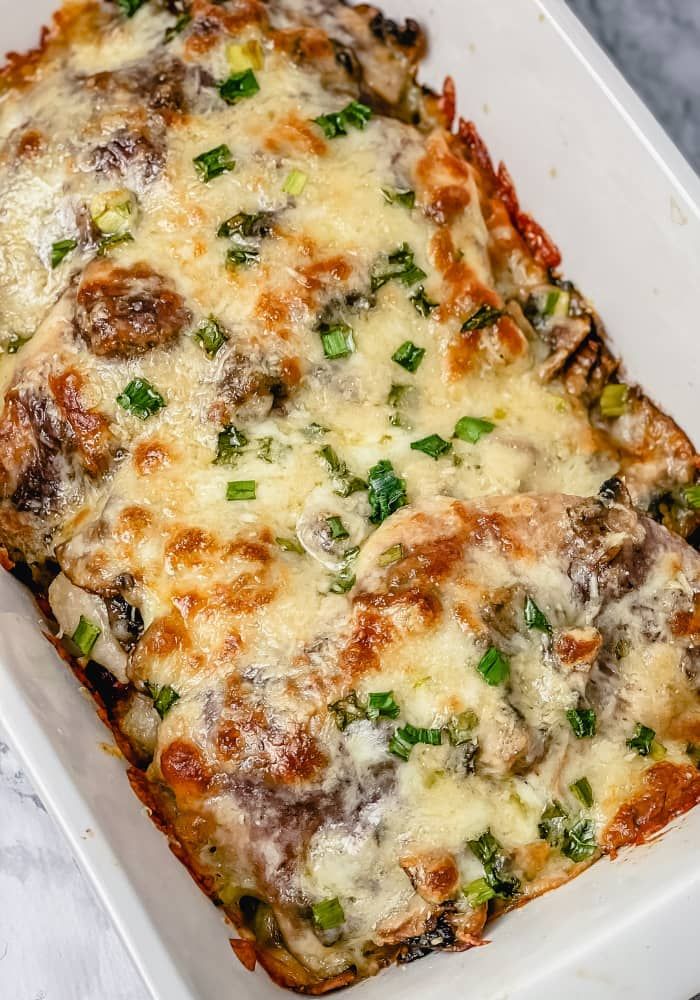 a casserole dish with meat, cheese and green onions in it on a marble surface