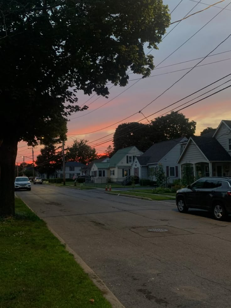 cars parked on the side of an empty street at sunset with power lines above them