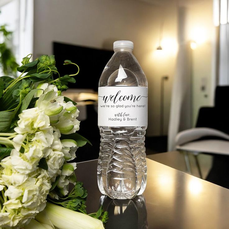 a bottle of water sitting on top of a table next to white flowers and greenery