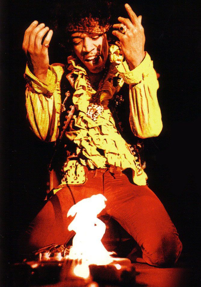 a man sitting on top of a stage holding his hands up in the air while wearing red pants