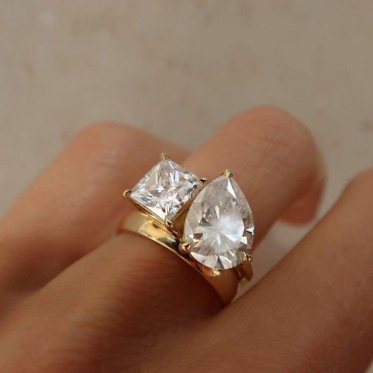 a woman's hand with two engagement rings on top of her finger and the ring is in yellow gold