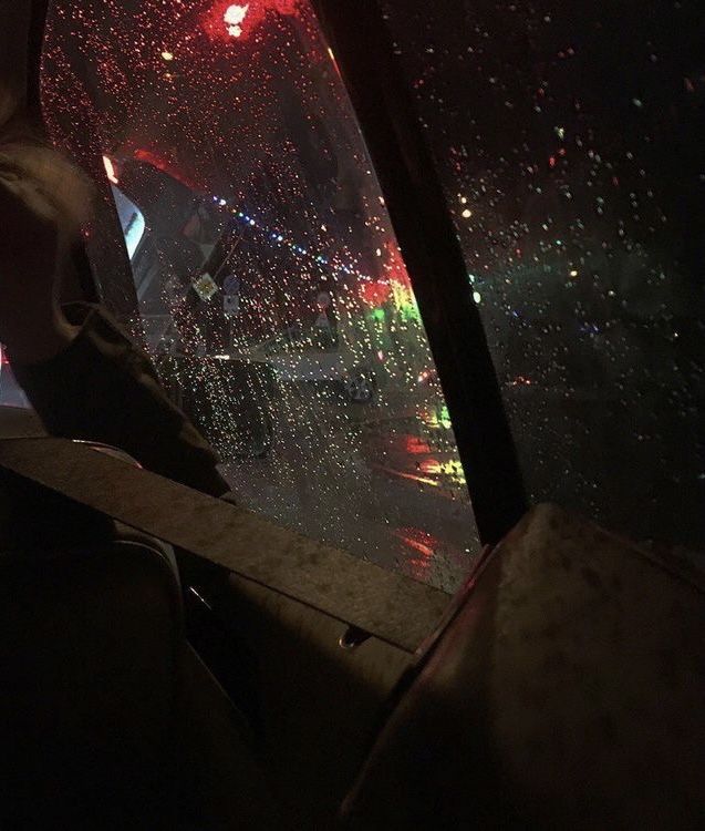 a person sitting in the passenger seat of a car on a rainy night with red and green lights