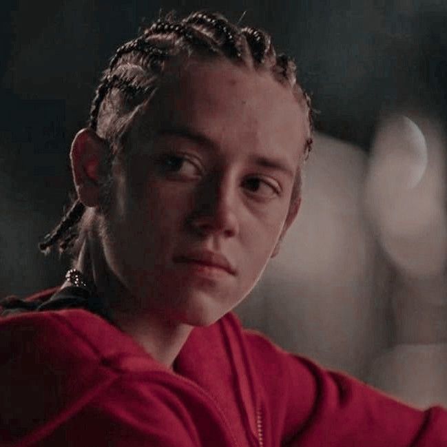 a woman with braids on her hair in a red shirt looking at the camera