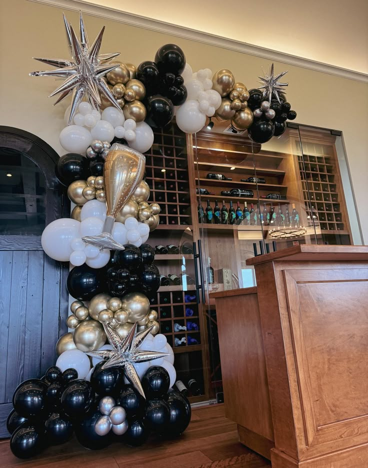 a large balloon arch is decorated with black, white and gold balloons