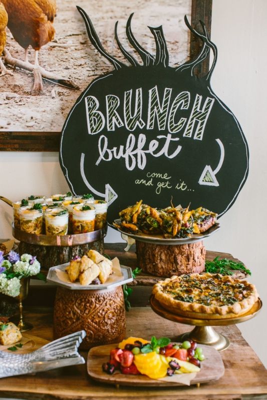 a table topped with lots of cakes and pies next to a chalkboard sign