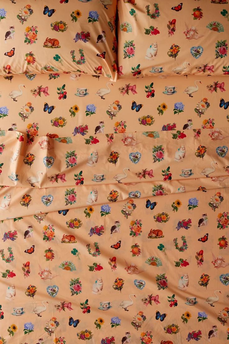 an unmade bed covered in lots of colorful flowers and butterflies on peach colored sheets