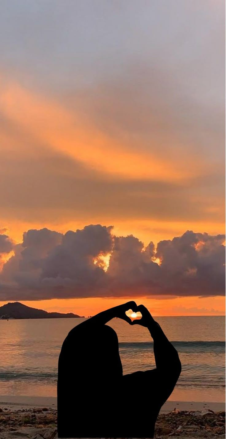 a man sitting on top of a beach next to the ocean with his hands up in the air