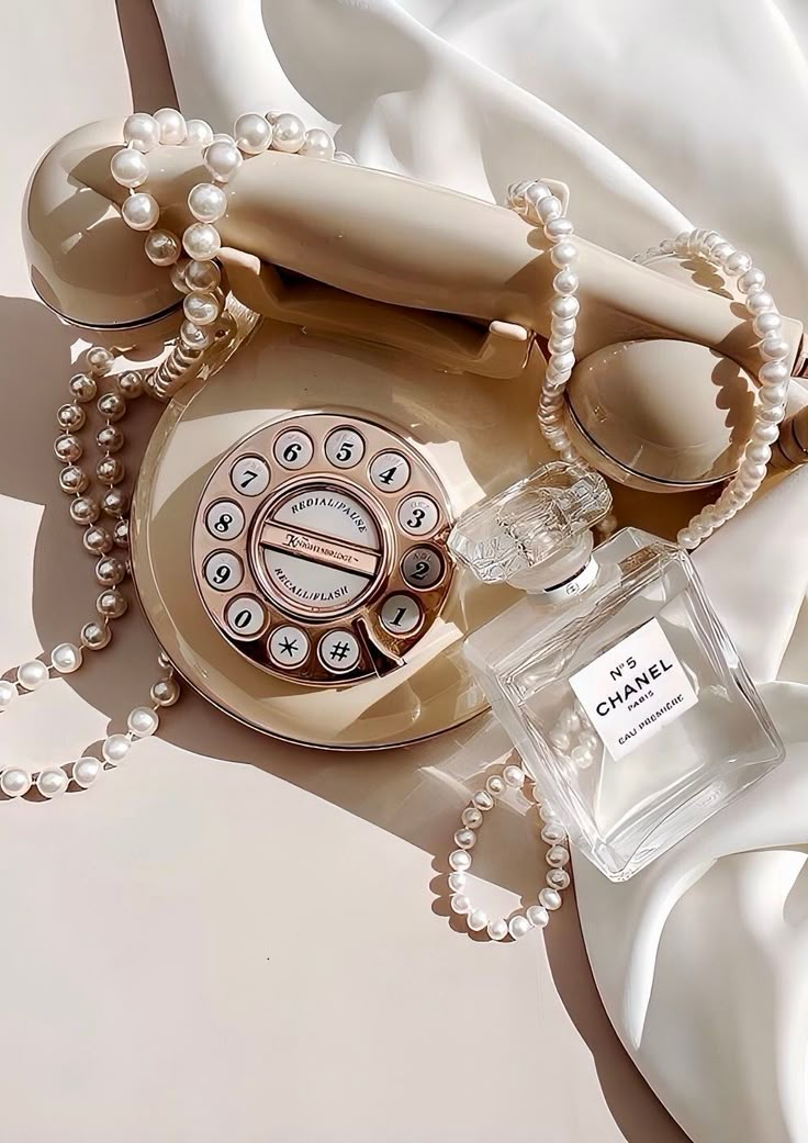 an old fashioned telephone and pearls on a white cloth with a bottle of chanel