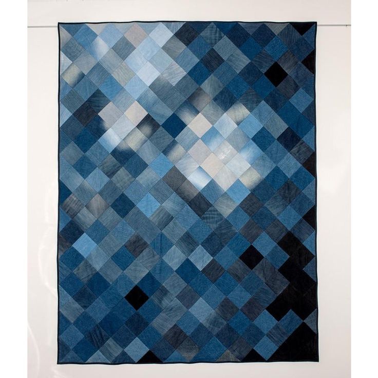 a blue and black patchwork quilt hanging on a white framed piece of art in a room